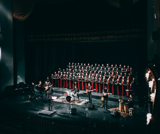 Photo by Sam Moghadam people standing on stage in front of red curtain